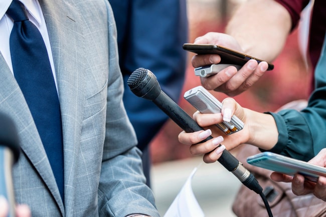 journalister håller fram mikrofon och mobiler till man med kostym