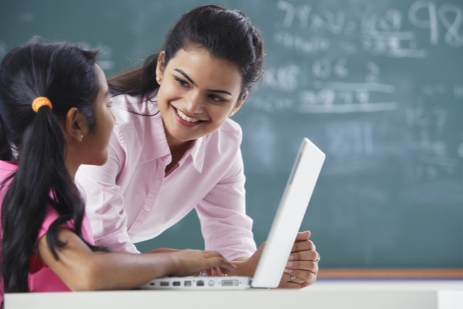 kvinna samtalar med en flicka vid dator i ett klassrum