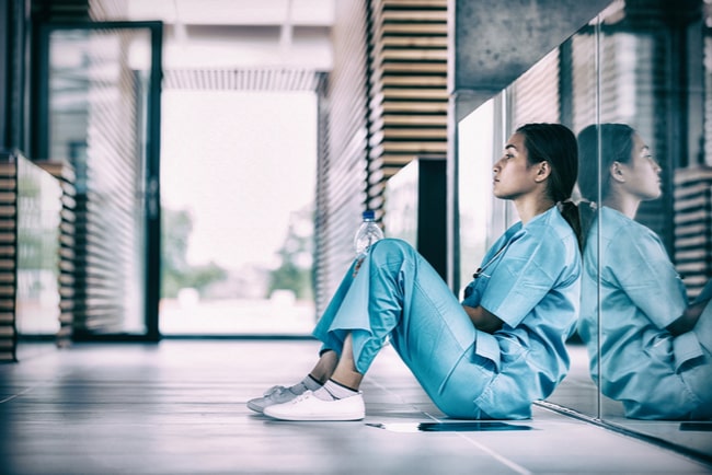 trött sjuksköterska sitter på golvet i en sjukhuskorridor