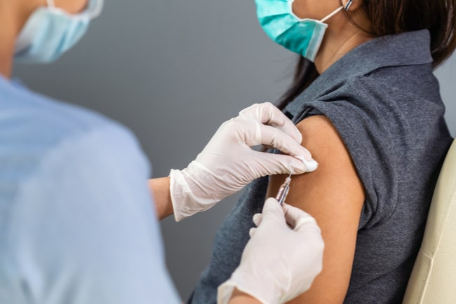 vårdpersonal med handskar och munskydd håller vaccinationsspruta mot patients arm