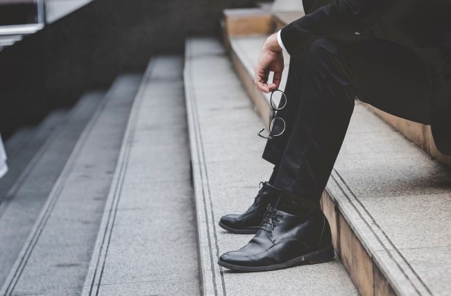 När bild på person i kostym som sitter i stentrappa med glasögon i händerna, koncept arbetslöshet, ekonomisk kris.